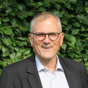 Porträt von Dirk Schmülgen vor einem Hintergrund mit Pflanzen.