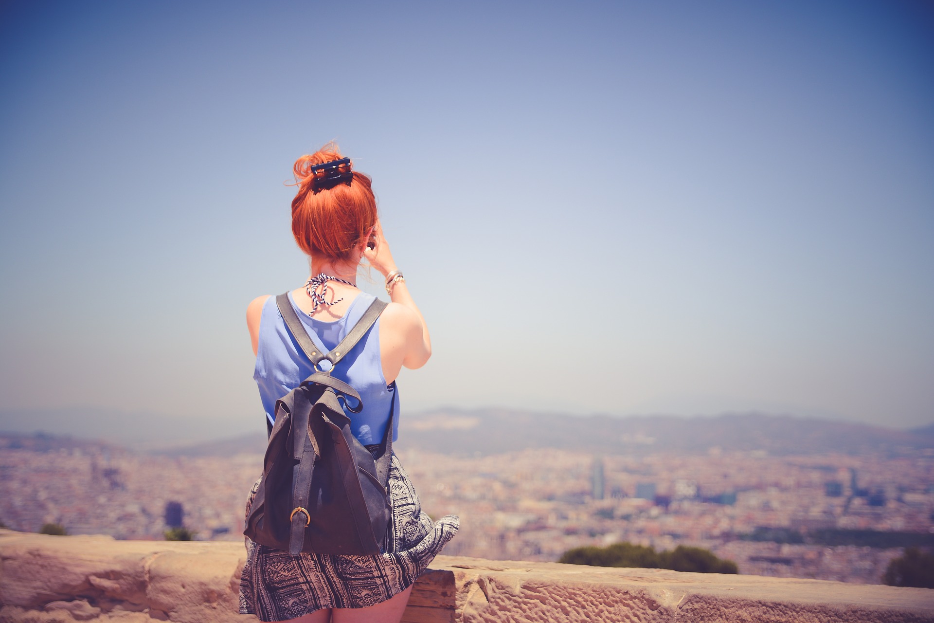 Ein junge Frau steht an einem Aussichtspunkt und fotografiert den Ausblick.